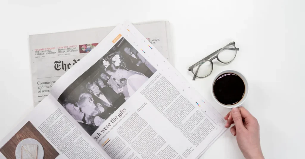 Overhead view of newspaper reading with coffee and glasses on a white table.